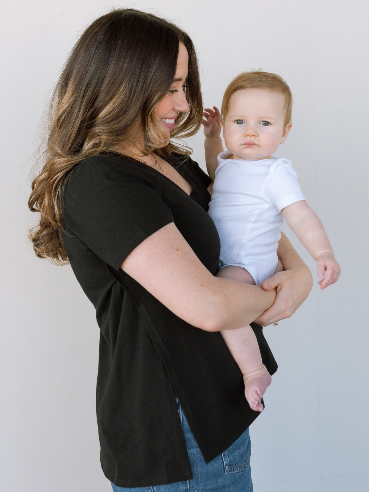 A woman holding her baby close and wearing a black nursing tshirt.