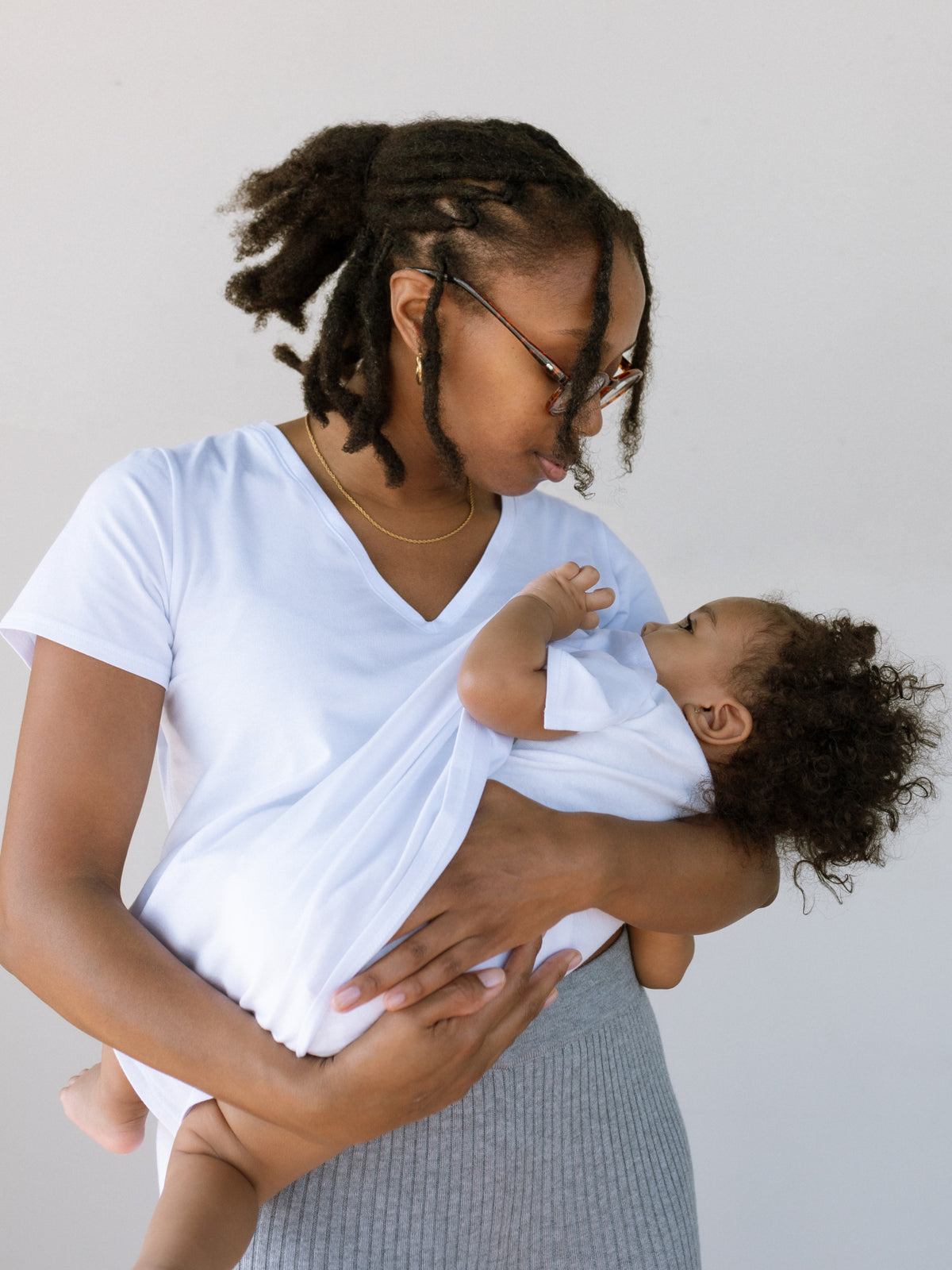 White v-neck nursing t-shirt with discreet nursing access. Modeled by a woman standing and breastfeeding her baby.